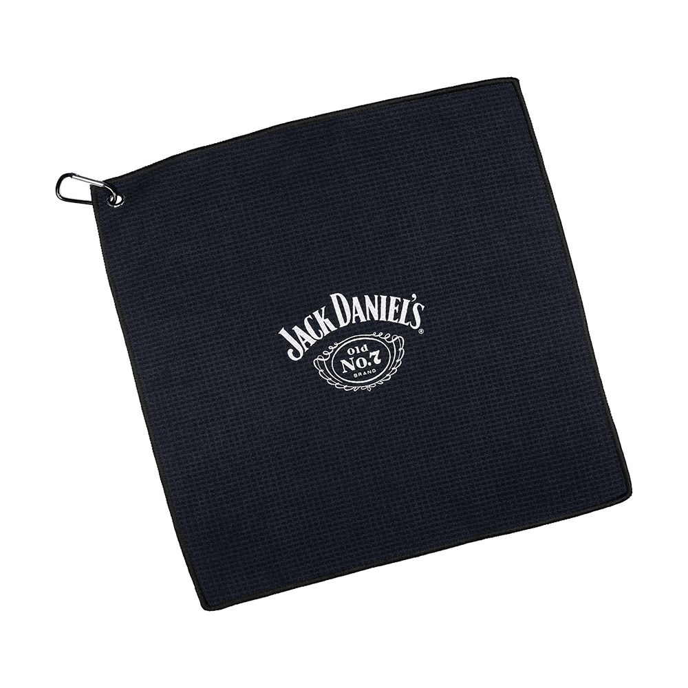 JD7032_Mission_Jack_Daniels_Handtuch_1 Dies ist ein schwarzes Handtuch mit dem weißen Jack Daniel's Logo in der Mitte. In der Ecke befindet sich eine Metallöse mit einem Haken zum Aufhängen.