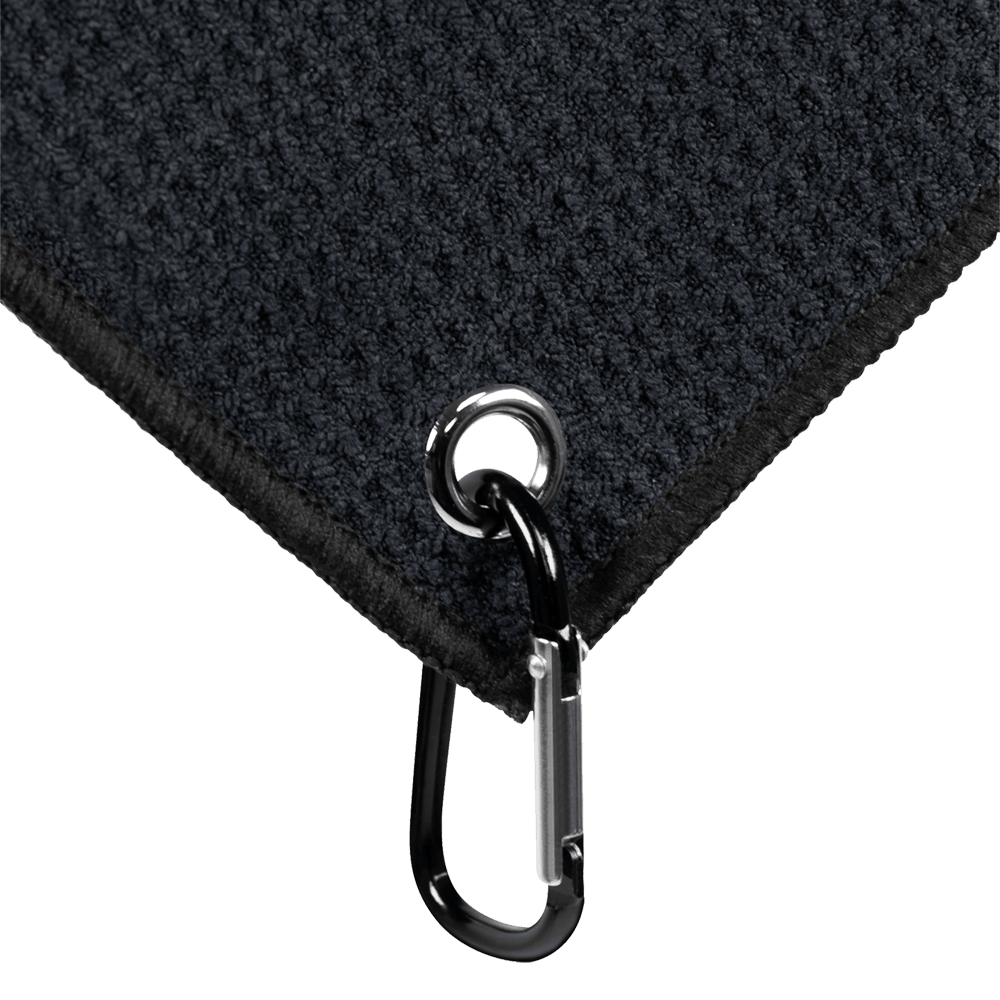 JD7032_Mission_Jack_Daniels_Handtuch_3 Das Bild zeigt eine Ecke eines schwarzen Handtuchs mit einer Öse und einem Karabinerhaken. Das Produkt heißt "Mission Jack Daniels Handtuch".