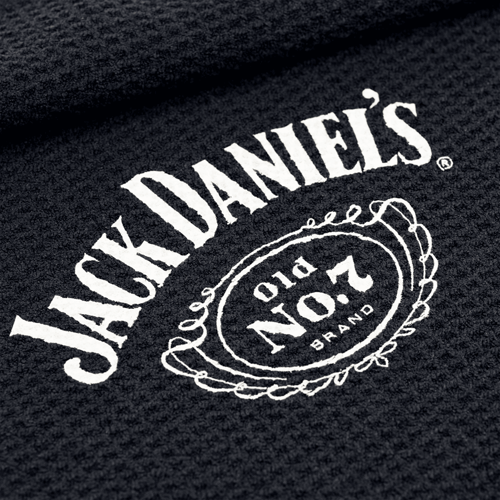 JD7032_Mission_Jack_Daniels_Handtuch_2 Das Bild zeigt ein schwarzes Handtuch mit dem weißen Jack Daniel's Logo darauf. Das bekannte "Old No. 7 Brand"-Design ist in der Mitte gut sichtbar.