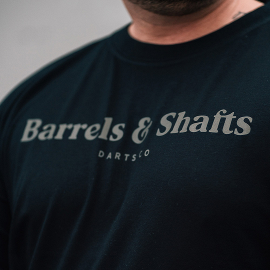 Barrels and Shafts T-Shirt - Black Das Bild zeigt ein schwarzes T-Shirt mit der Aufschrift "Barrels & Shafts". Darunter steht in kleineren Buchstaben "DARTSCO".