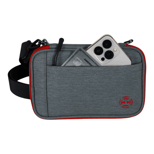 Harrows Smart Case XL dart wallet Das Bild zeigt eine graue Tasche mit rotem Rand und einem schwarzen Gurt. In der Vordertasche stecken ein Smartphone und eine Kreditkarte.