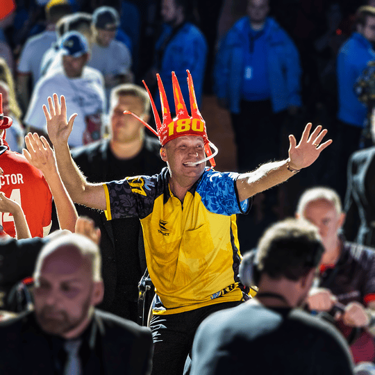 9026-McDart-180-er-Tr-tenkrone-5 Ein Mann trägt eine rote "McDart 180-er Trötenkrone" und jubelt in einer Menschenmenge. Er sieht fröhlich aus und ist von vielen anderen Fans umgeben.