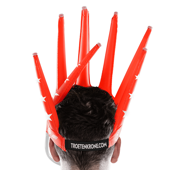 9026-McDart-180-er-Tr-tenkrone-3QhBeOlKOPs3Ze Eine Person trägt eine auffällige, rote, aufblasbare Krone mit mehreren Spitzen auf dem Kopf. Auf der Rückseite steht der Schriftzug "TROETENKRONE.COM".